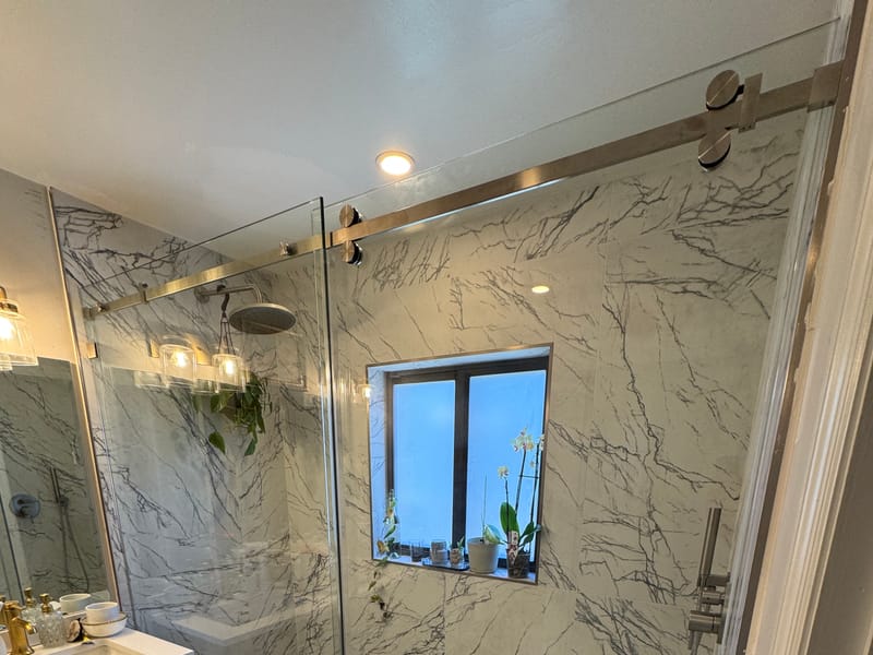 Frameless bypass shower door installed by Castilla Glass in a marble bathroom