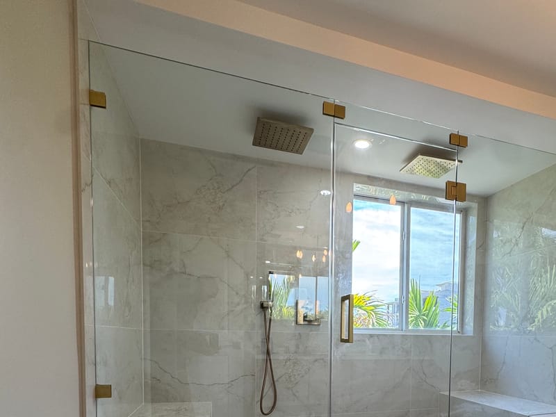 Frameless hinged shower enclosure with brass hardware and a bench