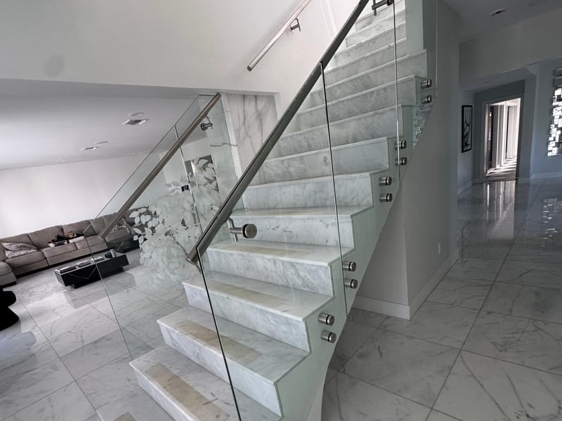 Frameless glass stair railing on marble stairs with stainless standoffs, installed by Castilla Glass